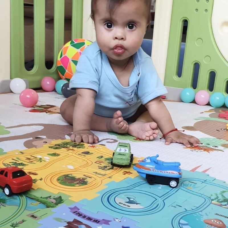 A joyful child smiling at the camera while playing with a colorful toy car track.