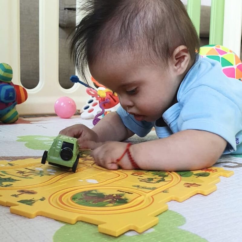 A happy child with Down syndrome playing with a colorful toy car in a sunny park.